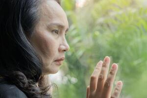 Close-up side view portrait of stressed woman 50 years old sitting near window thinking. photo