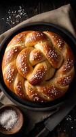 Braided pretzel with coarse salt lies on a round black platter photo