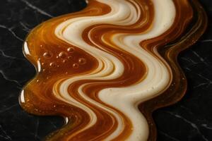 Viscous golden honey and creamy white milk swirling together on a black marble surface photo