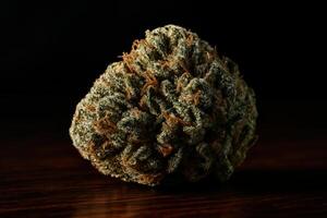 High detail macro shot of a single cannabis bud on dark wood, showing trichomes and orange hairs photo