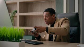 Funny office worker happy African American man employee gamer hold controller joystick playing computer game male businessman play console football videogame gaming addiction having fun at work video