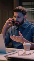 Businessman Indian guy multitasking business man male in night late office overtime work talking mobile phone call discuss computer laptop commerce smartphone conversation smiling manager consulting video