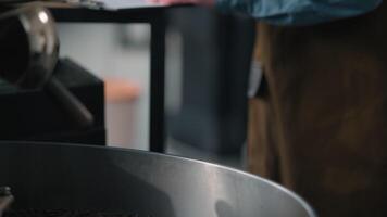 Coffee roasting factory Caucasian man barista in apron control roasted aroma caffeine fresh beans in roaster machine industry equipment check quality writing notes thoughtful male inspect thinking video