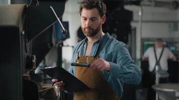 Caucasian man check coffee roasted aroma beans roaster machine equipment expert technologist inspect industry fresh caffeine roasting male guy writing notes checking quality go away control factory video