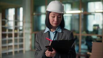 Builder woman Asian girl architect inspector in hard hat inspecting building construction checklist writing document industry plan Japanese Korean Chinese female engineer expert developer foreman work video