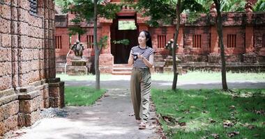 Handheld shot, Cheerful woman is enjoying a quiet stroll, taking photos of old sculptures and ancient brick structures, Enjoy holiday travel. video