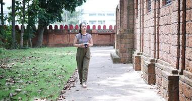 Handheld shot, Cheerful young woman is enjoying a quiet stroll, taking photos of old sculptures and ancient brick structures, Enjoy holiday travel. video