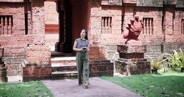 Handheld shot, young woman is enjoying a quiet stroll, taking photos of old sculptures and ancient brick structures, Enjoy holiday travel. video