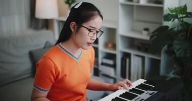 Handheld shot, A young Asian woman is happily playing a keyboard in a cozy living room. Enjoy favorite musical instruments video