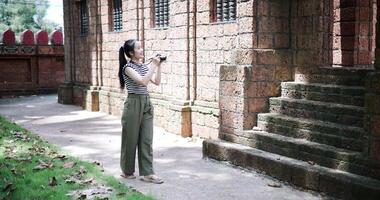 Handheld shot, Asian woman is enjoying a quiet stroll, taking photos of old sculptures and ancient brick structures, Enjoy holiday travel. video