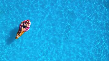 Young woman enjoying vacation while relaxing on a mattress in a swimming pool. Concept freedom, summer relaxation. Shot from drone video