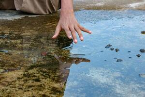 Hand Touching Water Surface in a Puddle Creating Ripples photo