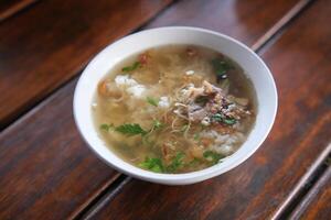 Bowl of Soto Ayam Chicken Noodle Soup on Wooden Table Surface photo