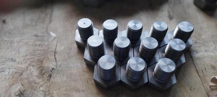 Close-up of a group of metal hex bolts arranged on a wooden surface. Hex head bolts arranged in a pattern. Metal hardware. Industrial fasteners with a shallow depth of field. Mechanical engineering. photo