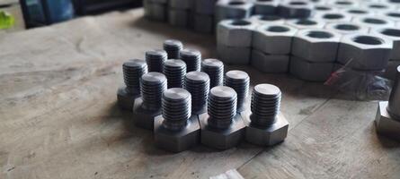 Close-up of a set of new metal bolts. Hex head bolts in focus, with nuts in the background. Industrial fasteners on a wooden surface. Selective focus with blurred background. photo