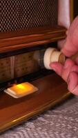 vertical Hand gently adjusts the tuning knob of a vintage wooden radio, bathed in the warm glow of its illuminated dial, evoking a sense of nostalgia and timeless audio experience video