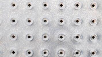 A silver metal surface with a pattern of small, evenly spaced circular indentations, each with a small black hole in the center photo