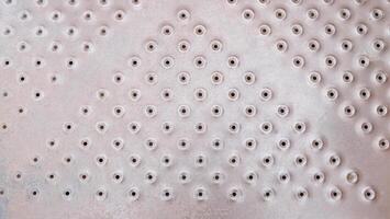 A gray surface with a pattern of small, evenly spaced holes, creating a textured and perforated appearance, industrial design photo