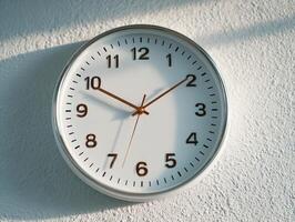 White clock showing time on textured wall in sunlight photo