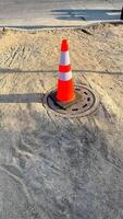 Neon cone guarding the shadowy manhole, urban sentinel of underground mysteries, celebrating Obscura Day and Street Safety Week photo