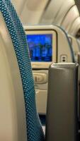 Snug teal airplane seats whisper wanderlust dreams, in flight screen flickering exotic landscapes, Digital Nomad Day anticipation photo