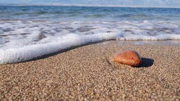 Single rock on sand beach, wave foam splash slow motion video