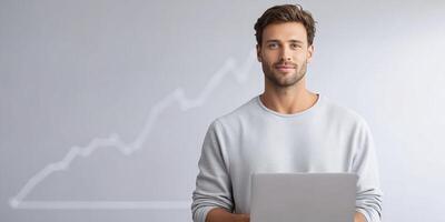 Young man with laptop, wearing casual gray sweater, stands confidently in front of a light background with upward trend graph, symbolizing business success and growth potential photo