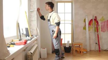 Construction worker using pencil and ruler to take measures on a wall, preparing for home improvement in a room with tools and materials, during apartment renovation video