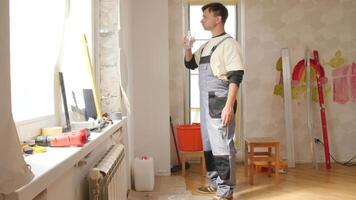 Construction worker taking a break, drinking water and looking out the window in a room being renovated, with tools and materials scattered around video