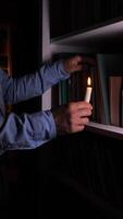 vertical Man holding candle is choosing a book from a bookshelf in a dark room, symbolizing knowledge, learning, and the pursuit of wisdom in challenging circumstances video