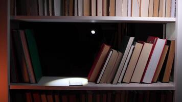 burglar steals dollar banknotes inside a hollowed-out book on a library bookshelf, using a flashlight to navigate the dark surroundings during the night video