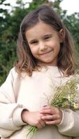 Happy child holding a vibrant bouquet of wildflowers, enjoying a sunny day in a lush green meadow, surrounded by flourishing plants and trees, radiating joy and innocence video