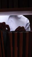 vertical Close-up view of a librarian searching through books on a shelf in a dimly lit library, selecting a volume either for a customer or personal reading enjoyment video
