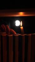 vertical Hand holding a burning white candle, casting a warm glow across a bookshelf filled with books in a dark room, creating an inviting and mysterious ambiance perfect for quiet reading video