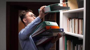 Young office worker carrying a stack of ring binders while searching for important documents in the company archive, navigating through shelves filled with organized paperwork video