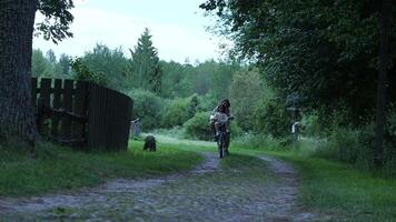 Mother and daughter riding bicycles along a scenic rural road, surrounded by lush trees and a rustic wooden fence, cherishing joyful moments together in serene nature video