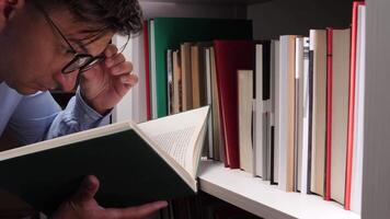 Researcher engrossed in reading a book while standing beside a bookshelf filled with publications, reflecting a commitment to learning and academic pursuit video