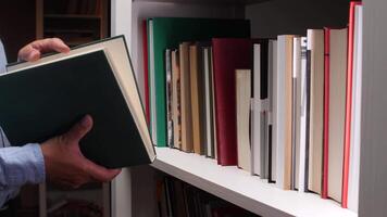 Close-up of a librarian's hands carefully placing a dark green hardcover book onto a white bookshelf filled with various colorful books, creating a vibrant and organized display video