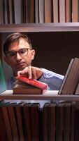 vertical Librarian secretly counting dollar banknotes hidden between books in the library after working hours, perhaps involved in illegal activities of buying and selling rare volumes video