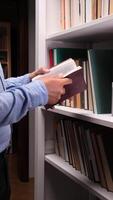 vertical Close up of male hands holding dollar bills and hiding them behind books in a white library bookshelf, suggesting secret savings, illegal activities, or hidden funds video