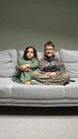 vertical Brother and sister are sitting on a comfortable sofa at home, watching a television program together, with a remote control resting beside them video