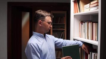 Male librarian holding a book while selecting another from the library bookshelf, deeply engaged in searching for valuable information and expanding knowledge through literature video