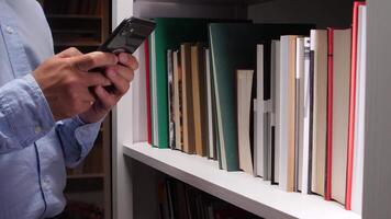 avvicinamento di un' bibliotecario utilizzando un' smartphone Il prossimo per un' bianca libreria, potenzialmente gestione il biblioteca inventario o ricerca per informazione video