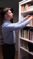 vertical Young man searching intently for a specific book among the organized shelves of a home library, surrounded by a diverse collection of literature and knowledge video