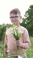 vertical Happy boy wearing glasses, holding a vibrant bouquet of wildflowers, smiling brightly while standing in a sunlit field on a warm summer day, enjoying the beauty of nature video