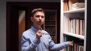 A man in a blue shirt is standing in front of a book shelf video