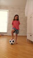 A young girl standing on a wooden floor with a soccer ball video