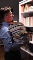 vertical Male librarian carefully placing book on shelf while holding stack of books, surrounded by numerous books in library or bookstore, showcasing organization and knowledge video