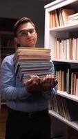 vertical portrait Male librarian carrying a large stack of books in a library, surrounded by bookshelves filled with literature, showcasing the abundance of knowledge and information available video