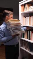 vertical Young male librarian struggling to carry a heavy stack of books while arranging bookshelves, making funny faces that reflect the effort and humor of the task at hand video
